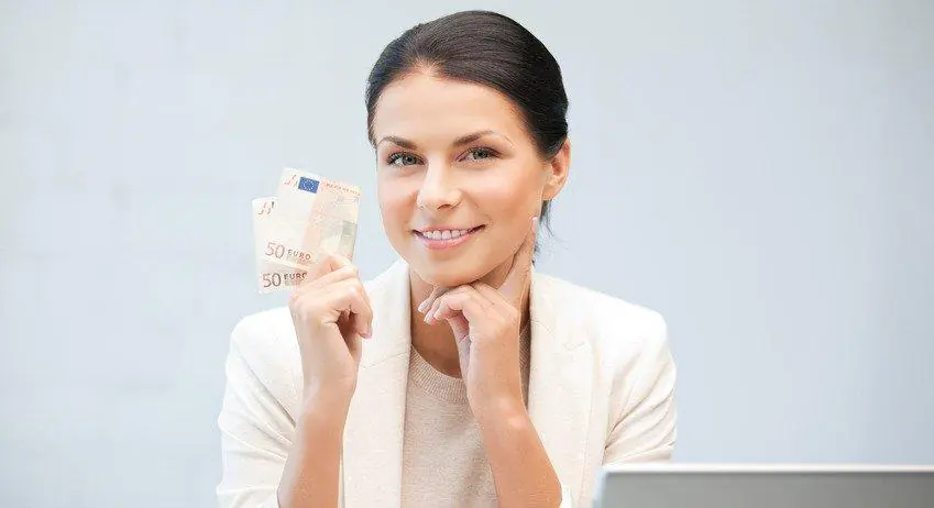 kobieta z banknotem w dłoni siedząca przed laptopem