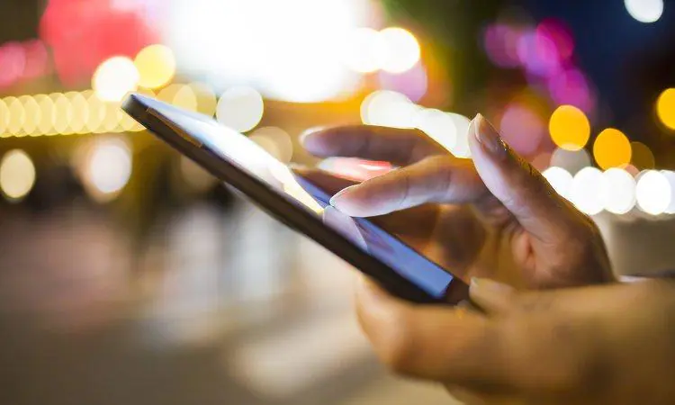 smartfon w kobiecych dłoniach na tle świateł miasta