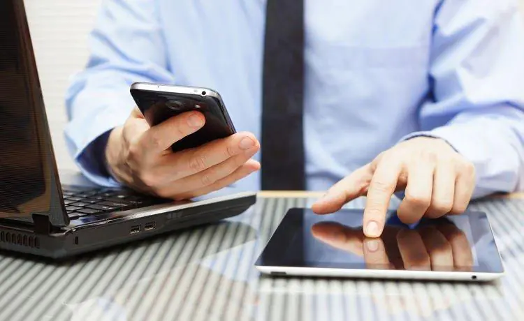 mężczyzna w niebieskiej koszuli pracujący na laptopie, smartfonie i tablecie