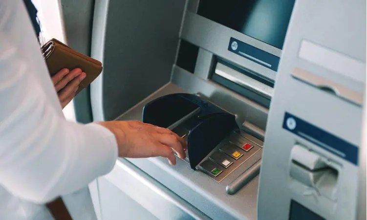 osoba w białej koszuli wypłacająca gotówkę z bankomatu