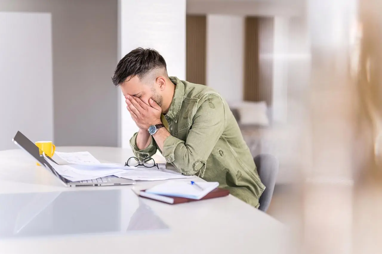 Załamany mężczyzna pochylony nad laptopem i dokumentami - po odrzuceniu wniosku o kredyt hipoteczny.