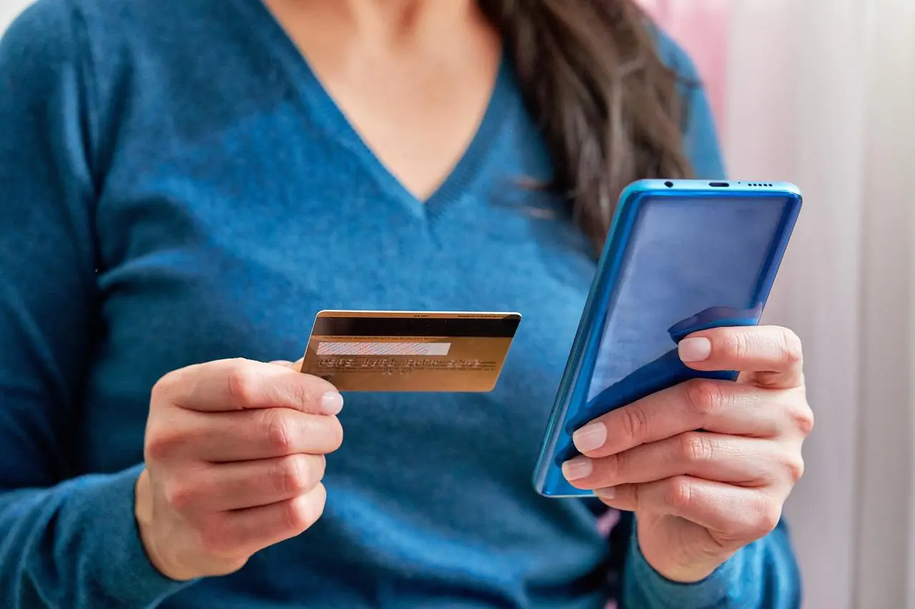 Kobieta trzyma w dłoniach kartę płatniczą i telefon komórkowy