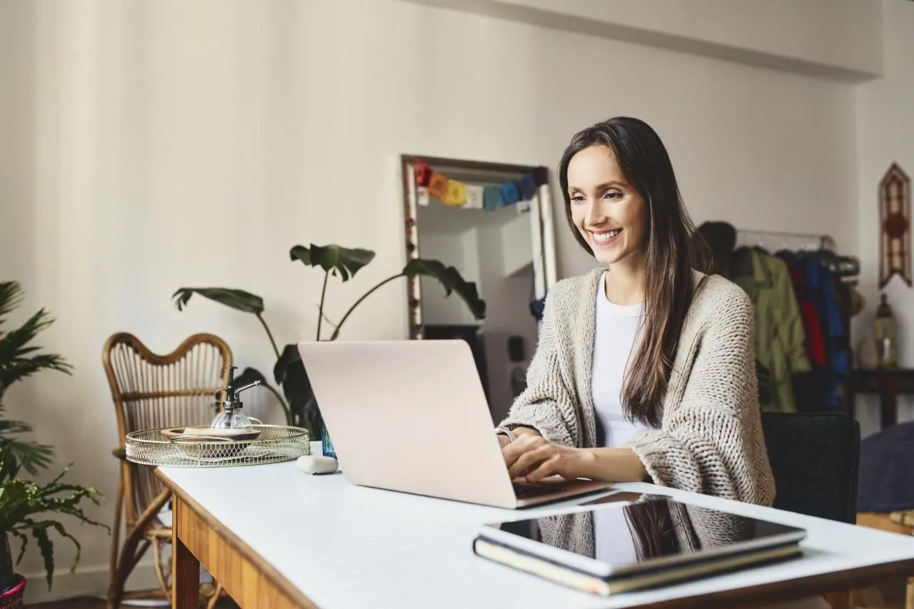 Zadowolona kobieta siedząca przed laptopem i wnioskująca o limit kredytowy.