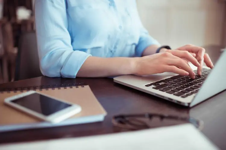 kobieta w niebieskiej koszuli pisząca na klawiaturze laptopa