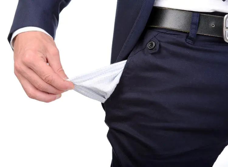 mężczyzna w granatowym garniturze wyciągający na zewnątrz pustą kieszeń spodni