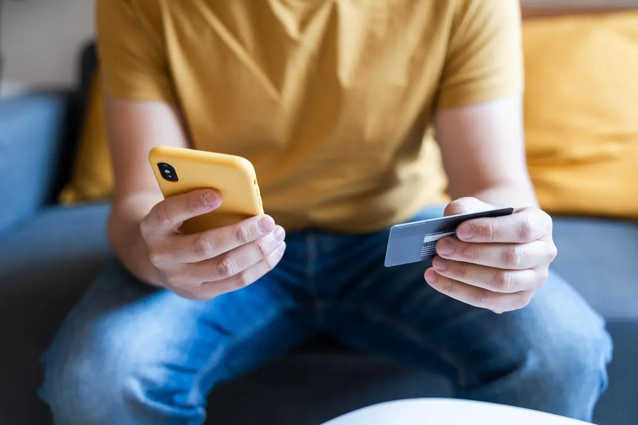Mężczyzna trzyma w rękach kartę płatniczą i telefon komórkowy