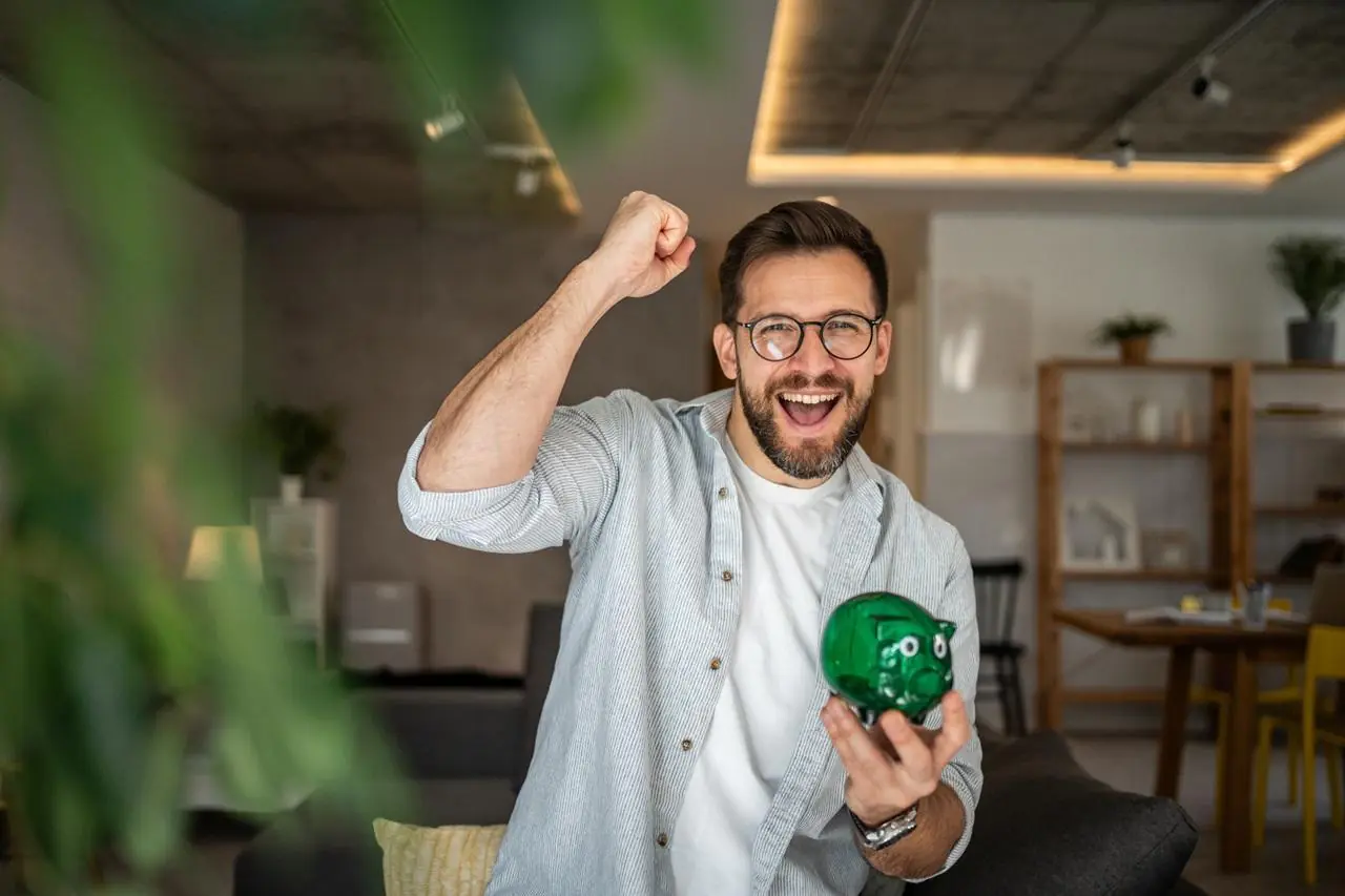 Mężczyzna w średnim wieku z zieloną świnką skarbonką w dłoni.