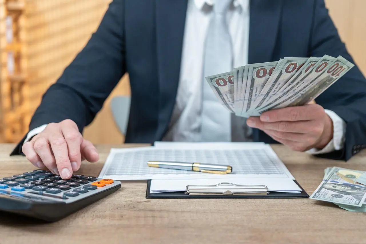 biznesmen z plikiem banknotów, kalkulatorem i umową udzielający pożyczki gotówkowej