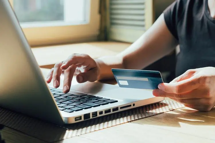 mężczyzna siedzący przy laptopie korzystający z karty kredytowej z debetem