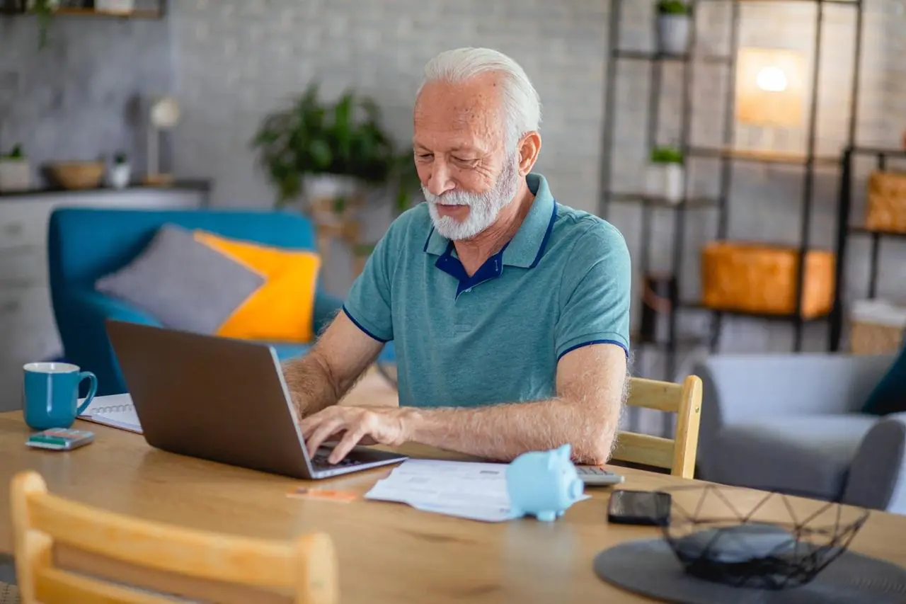 Starszy mężczyzna z laptopem sprawdzający na czym polega lokata na nowe środki online.