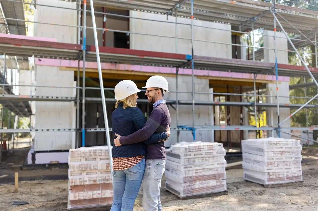 Małżeństwo w białych kaskach sprawdzające postępy na budowie domu jednorodzinnego.