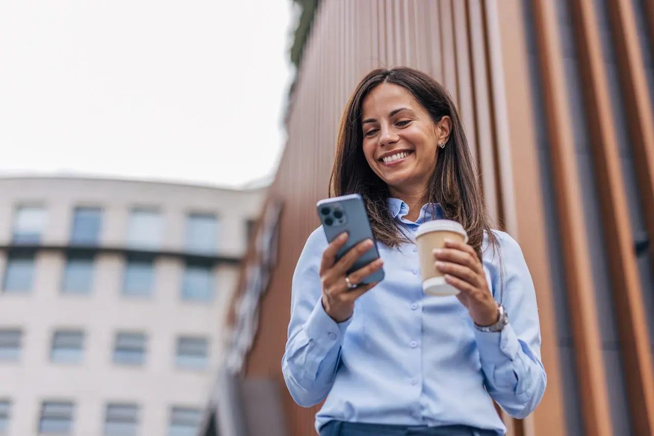 Zadowolona, młoda kobieta w błękitnej koszuli odbierająca na smartfonie czek BLIK