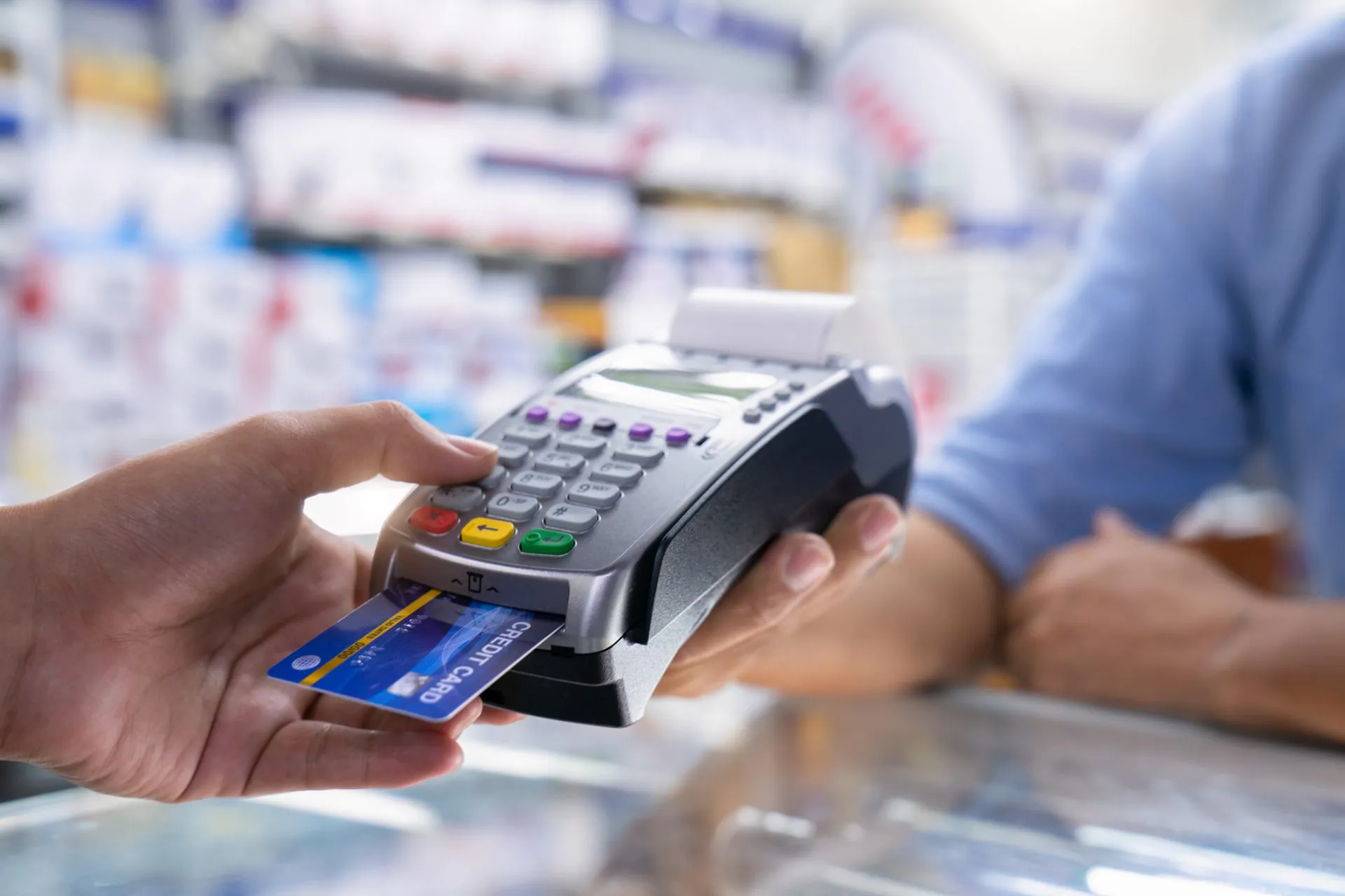 Zbliżenie na męską dłoń i terminal w trakcie płatności kartą w sklepie.
