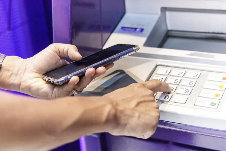mężczyzna trzymający w dłoni smatrfon sprawdza, jak działa wypłata BLIK z bankomatu