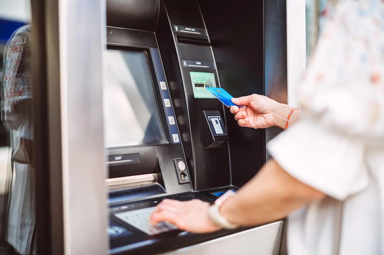 Zbliżenie na kobietę, która stoi z kartą przy bankomacie i sprawdza, jak wypłacić pieniądze