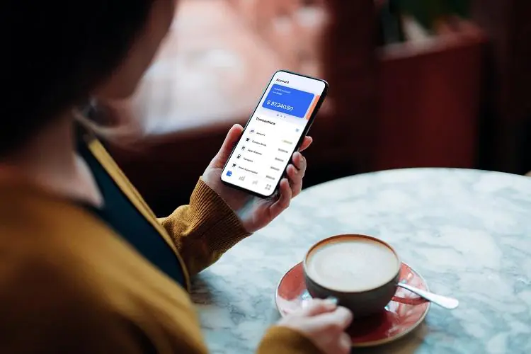 Kobieta w kawiarni sprawdza stan konta na telefonie