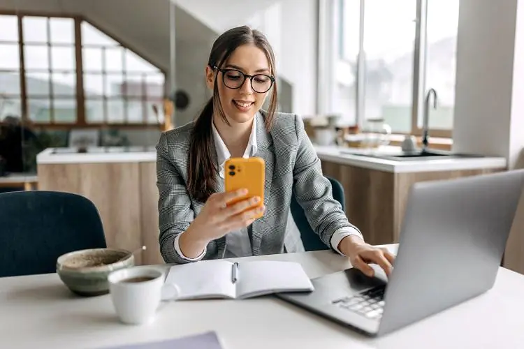 młoda kobieta siedząca przy biurku i sprawdzająca na smartfonie ranking pożyczek 1800 zł