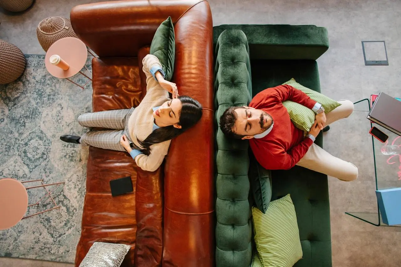 Mężczyzna i kobieta pokłóceni siedzą na dwóch kanapach tyłem do siebie.