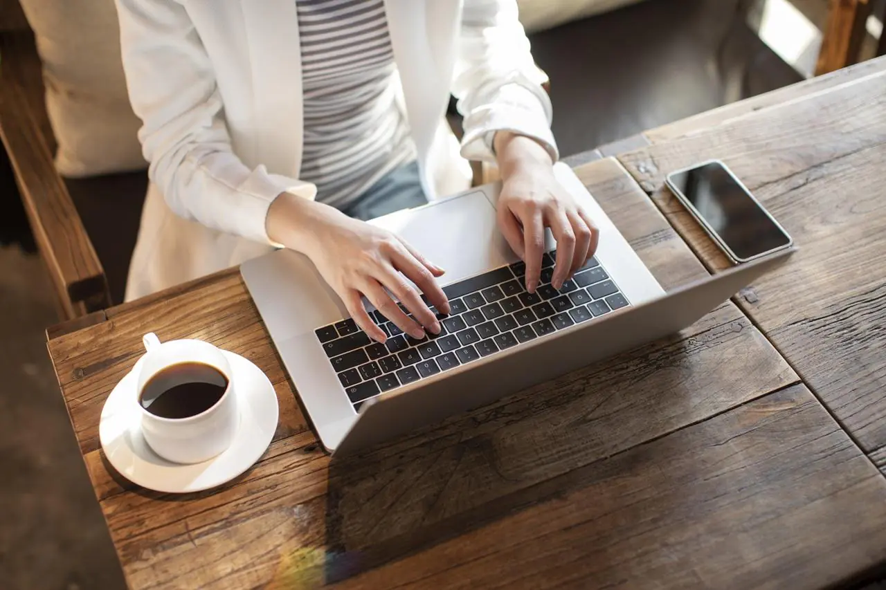 kobieta siedząca przy laptopie z kawą i zlecająca przelew z Nest Banku