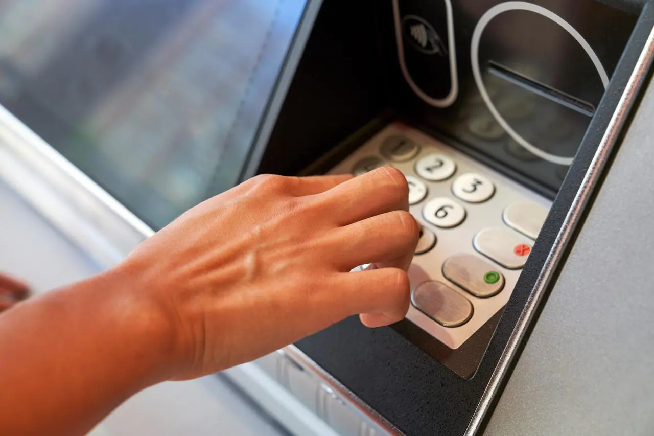 Mężczyzna wypłaca pieniądze z bankomatu