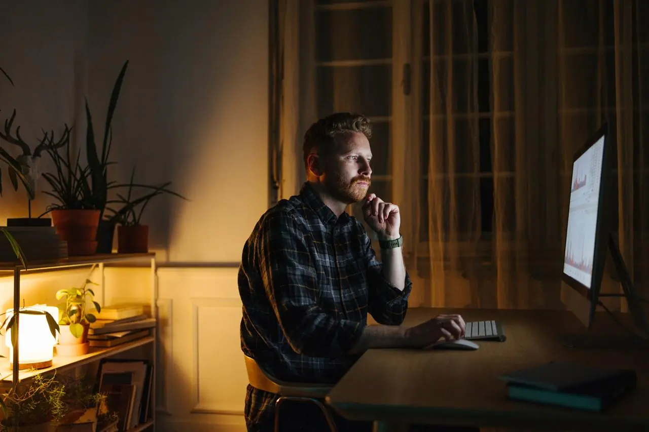 Młody mężczyzna siedzący nocą przed komputerem i sprawdzający, jak pracuje lokata overnight