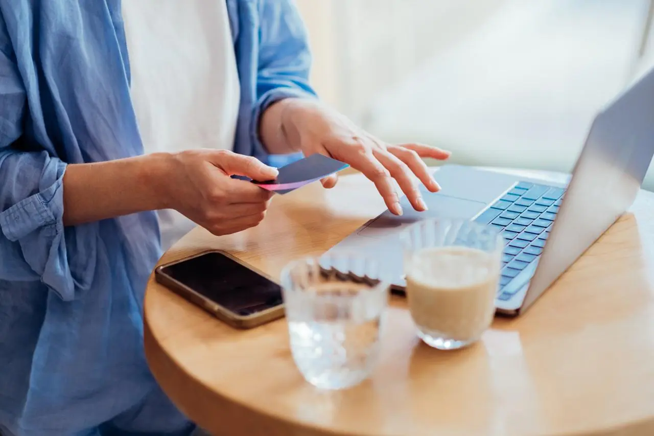 Zbliżenie na dłonie kobiety i laptop podczas wykonywania płatności kartą w internecie.