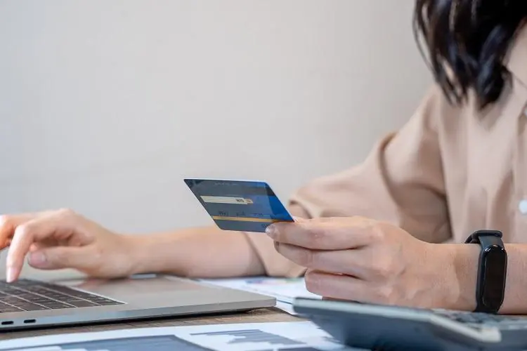 kobieta siedząca przy laptopie z kartą płatniczą i zlecająca przelew na Ukrainę