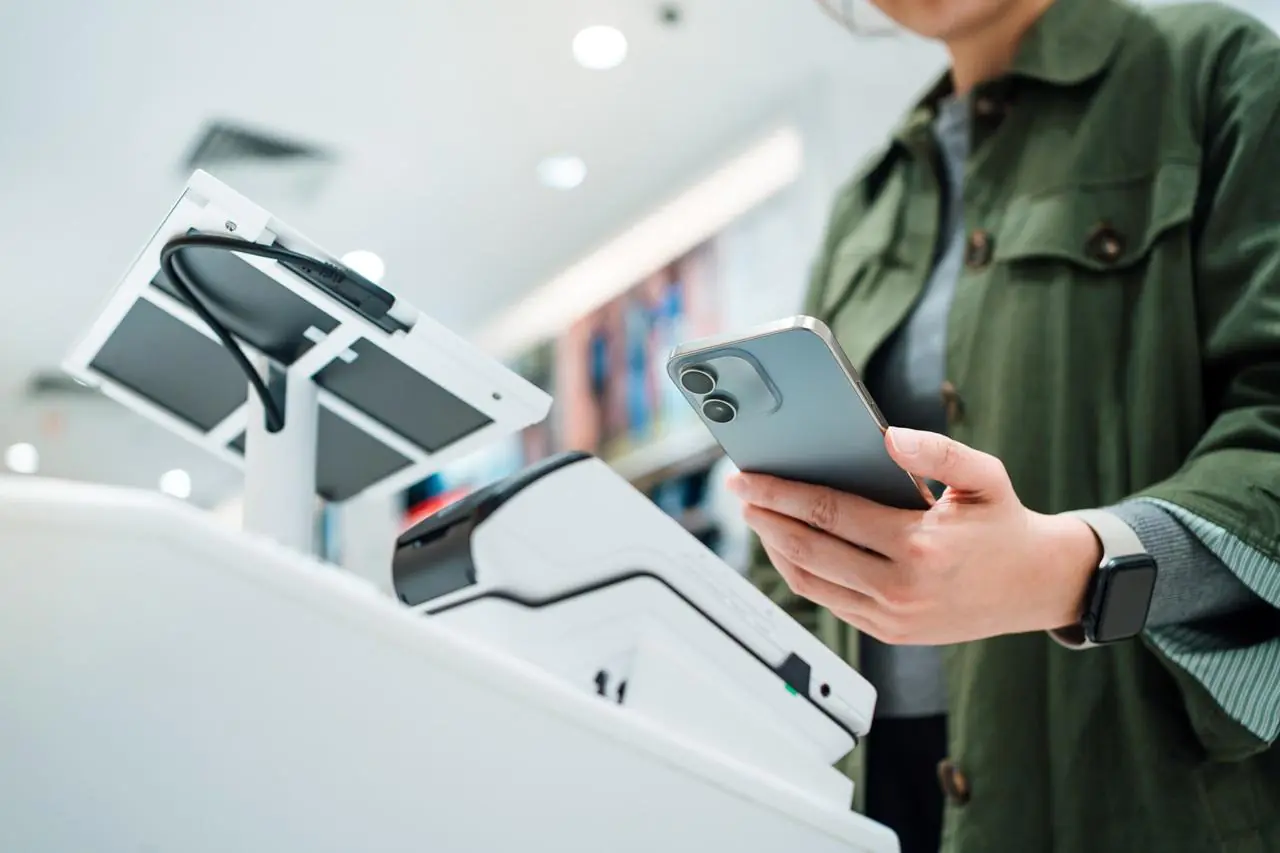 kobieta w zielonej koszuli płacąca blikiem zbliżeniowym za pomocą swojego smartfonu