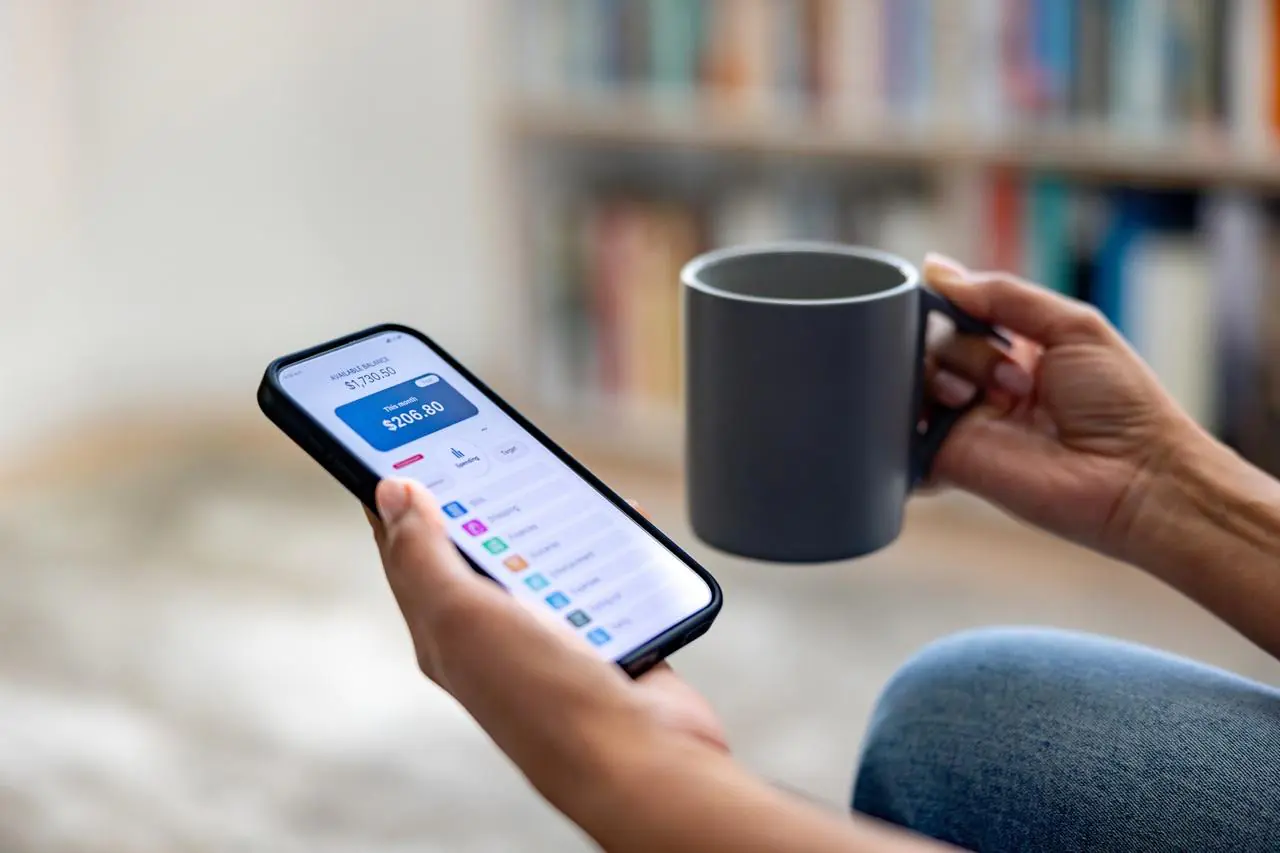 Zbliżenie na dłoń kobiety, która sprawdza na swoim smartfonie subkonto w banku