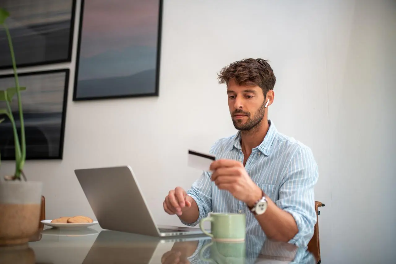 Młody mężczyzna siedzący przed laptopem i sprawdzający datę ważności karty.
