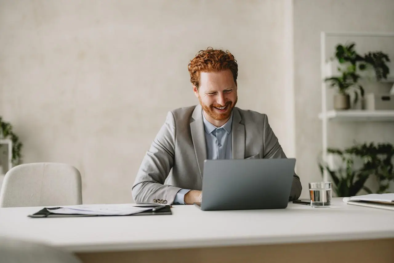 Zadowolony mężczyzna siedzący przed laptopem i sprawdzający najlepsze lokaty bankowe na 12 miesięcy.