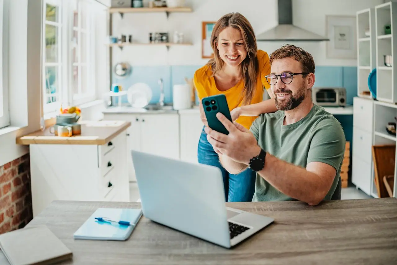 Młode małżeństwo przy stole z laptopem i smartfonem sprawdzające najlepsze lokaty bankowe na 12 miesięcy w rankingu online