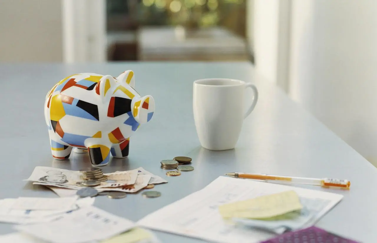 Kolorowa świnka skarbonka, banknoty, monety, kubek i dokumenty leżące na jasnym blacie