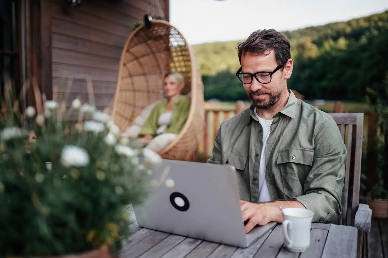 Mężczyzna siedzący z laptopem przed domem i sprawdzający ile kosztuje konsolidacja kredytu hipotecznego.
