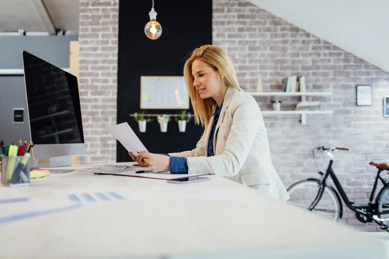 Młoda kobieta siedząca w biurze i sprawdzająca w umowie rachunku swój numer CIF.