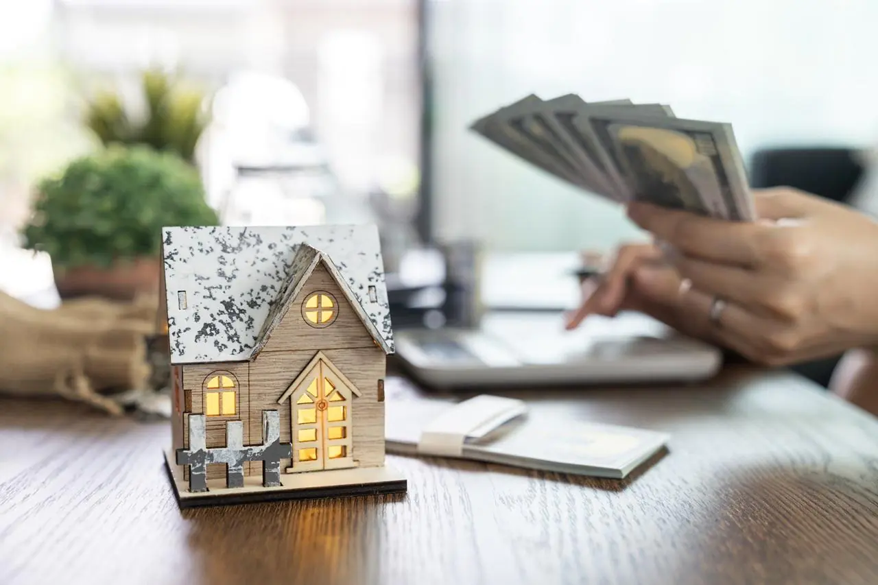 Model domu stojący na blacie a w tle osoba obliczająca ratę kredytu 200 tys zł na 10 lat