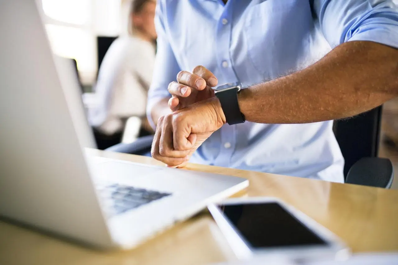 Mężczyzna pracuje na komputerze w biurze i sprawdza, która jest godzina