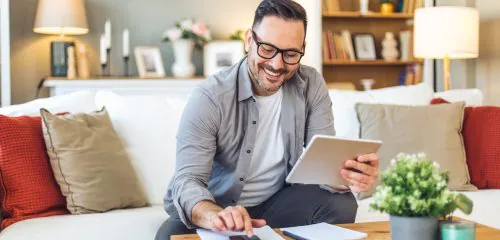 Uśmiechający się mężczyzna, siedzący w salonie i obliczający na kalkulatorze podatek Belki w 2026 roku.