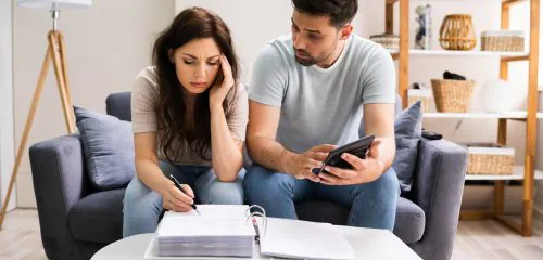 Zmartwiona para siedzi przy dokumentach z kalkulatorem i zastanawia się jak sobie poradzić ze spłatą kredytu