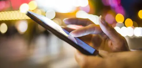 smartfon w kobiecych dłoniach na tle świateł miasta