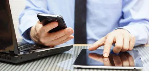 mężczyzna w niebieskiej koszuli pracujący na laptopie, smartfonie i tablecie