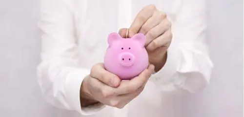 mężczyzna w białej koszuli trzymający świnkę skarbonkę