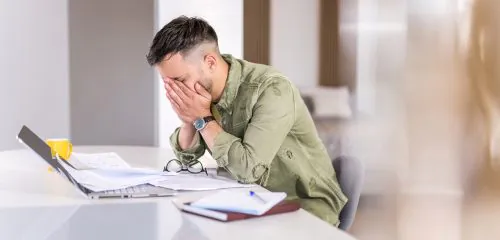 Załamany mężczyzna pochylony nad laptopem i dokumentami - po odrzuceniu wniosku o kredyt hipoteczny.