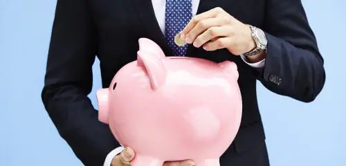 Mężczyzna w garniturze wrzuca monetę do świnki skarbonki