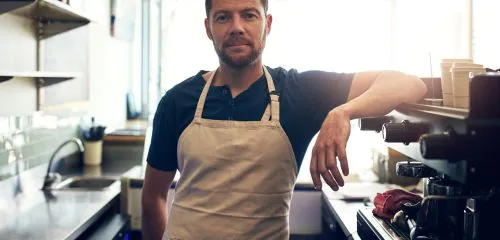 Mężczyzna w fartuchu w kawiarni przy maszynie do przygotowywania kawy