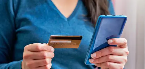 Kobieta trzyma w dłoniach kartę płatniczą i telefon komórkowy