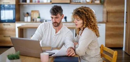 Młode małżeństwo siedzi przy laptopie i sprawdza, gdzie zaciągnąć kredyt konsolidacyjny dla zadłużonych