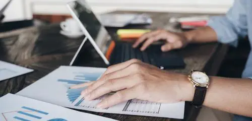 młody mężczyzna z zegarkiem na nadgarstku sprawdzający na laptopie ile trzeba zarabiać żeby dostać kredyt hipoteczny