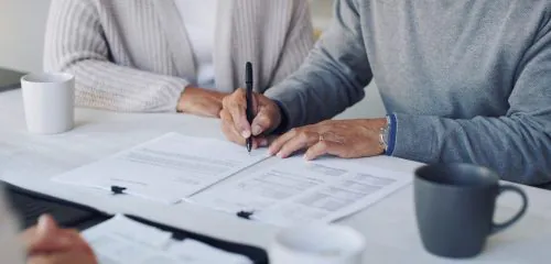 Starsze małżeństwo podczas wizyty w banku podpisuje odbiór promesy kredytowej.