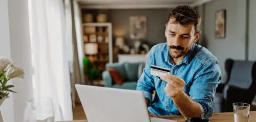 Mężczyzna w jeansowej koszuli sprawdza w internecie, czy jego karta kredytowa może być przeszkodą w zaciągnięciu kredytu hipotecznego